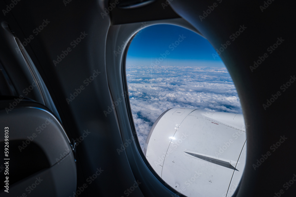 Commercial plane jet engine. Inside cabin-window view, blue sky, cloudy below, no people