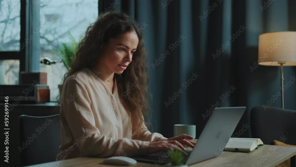 Side shooting of attractive young Caucasian woman with beautiful natural curly hair sitting at laptop and messaging with friends on social media. Weekend. Communication concept. Indoors Side shooting of attractive young Caucasian woman with beautiful natural curly hair sitting at laptop and messaging with friends on social media. Weekend. Communication concept. Indoors
