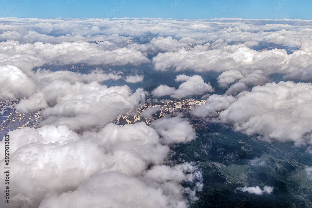 View from the stratosphere to a cloudy landscape over mountains covered with snow in summer. In the sky above storm cumulus clouds