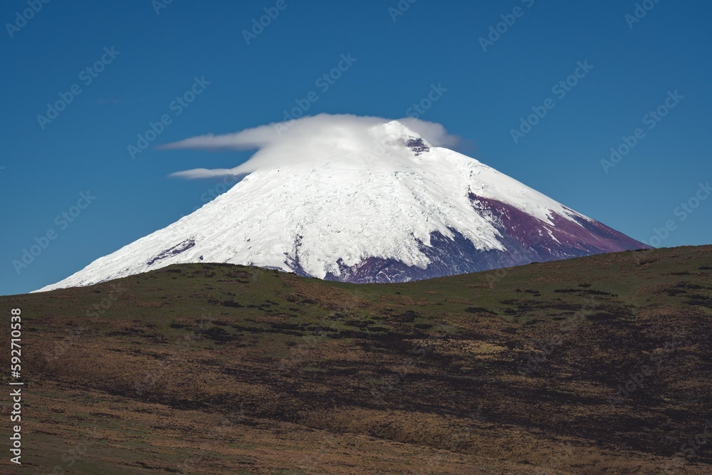 Layer of white fluffy clouds in front of snowy Cotopaxi volcano on blue sky background in Ecuador