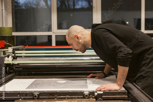 Tableau sur toile The artist is placing a paper stencil or template on a lithographic press or rolling press used for creating lithography in an art workshop