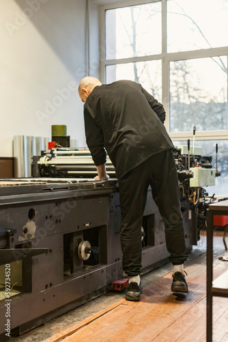 The artist standing next to a lithographic press, or rolling press in an art workshop.