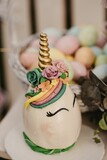 Vertical shot of a unicorn cake with colorful Easter eggs in the blurred background