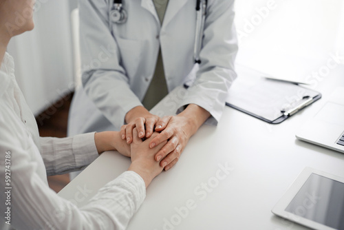 Doctor and patient sitting at the desk in clinic office. The focus is on female physician's hands reassuring woman, close up. Perfect medical service, empathy, and medicine concept © rogerphoto