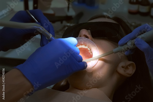 Dentist is preparing woman's teeth for installing ceramic veneers and crowns using drill. He is removing partly an enamel of the teeth. Dentistry, prosthetics concept. Treatment by an orthodontist.