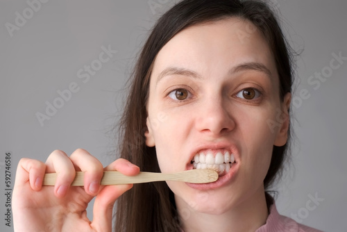 Smiling brunette woman with organic bamboo toothbrush and toothpasteis brushing her white teeth. Biodegradable ecological personal care products. Plastic free lifestyle concept.