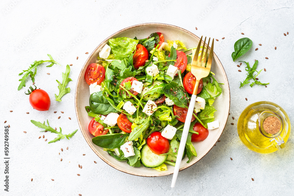 Spring salad in craft plate. Spinach, arugula, tomatoes and feta with olive oil. Top view on white. Spring salad in craft plate. Spinach, arugula, tomatoes and feta with olive oil. Top view on white.