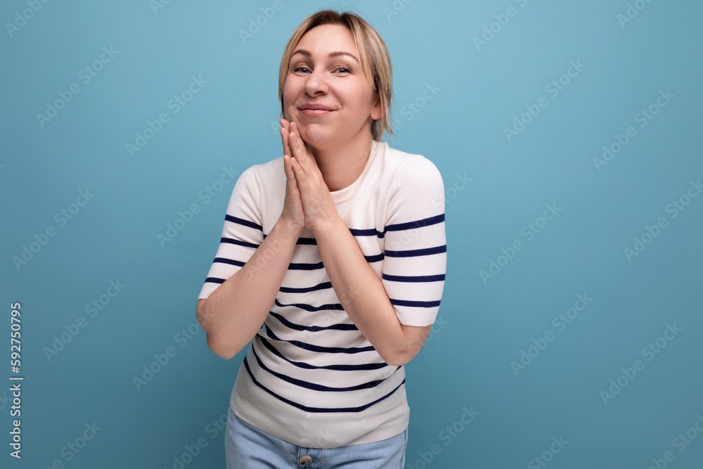 Obraz premium cute blond young woman in a striped sweater on a blue background with copy space