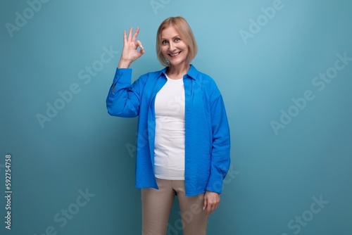joyful smiling 50s middle aged woman in a blue shirt on a blue background with copy space