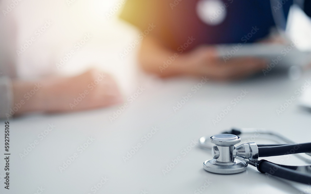 Stethoscope lying on the tablet computer in front of a doctor and patient at the background. Medicine, healthcare concept