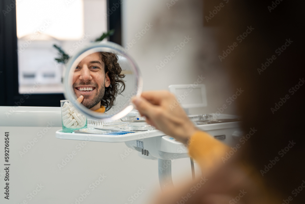 Φωτογραφία Handsome young man looking at mirror at dentist checking results after dental treatment teeth whitening new veneers feeling happy and satisfied, confident with healthy teeth smile
