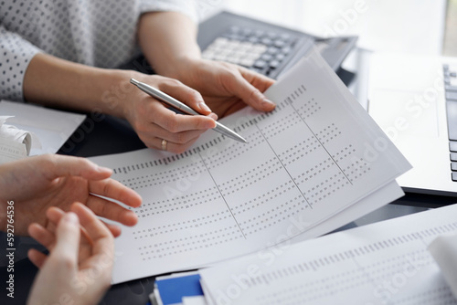 Female accountant pointing with a pen into audit paper while explaining tax counting results, close up. Business audit and finance concepts