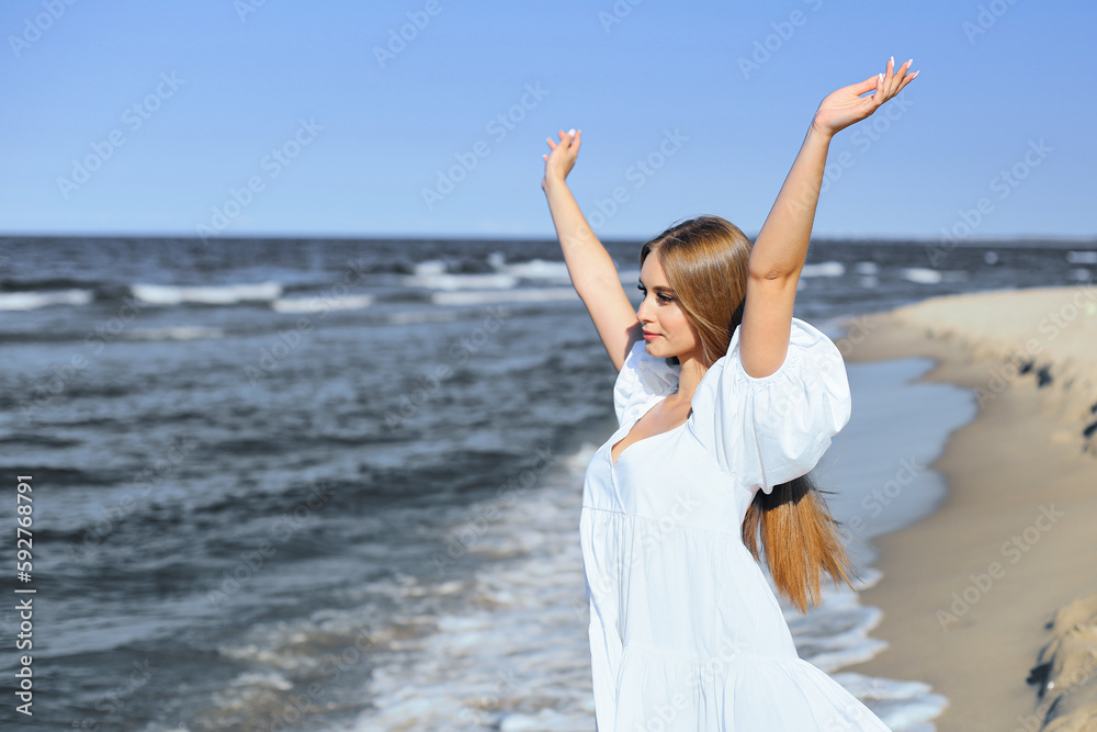 Happy, beautiful woman on the ocean beach standing in a white summer dress, raising hands Happy, beautiful woman on the ocean beach standing in a white summer dress, raising hands