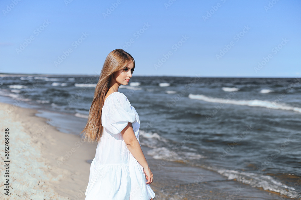 Happy, beautiful woman on the ocean beach standing in a white summer dress. Portrait