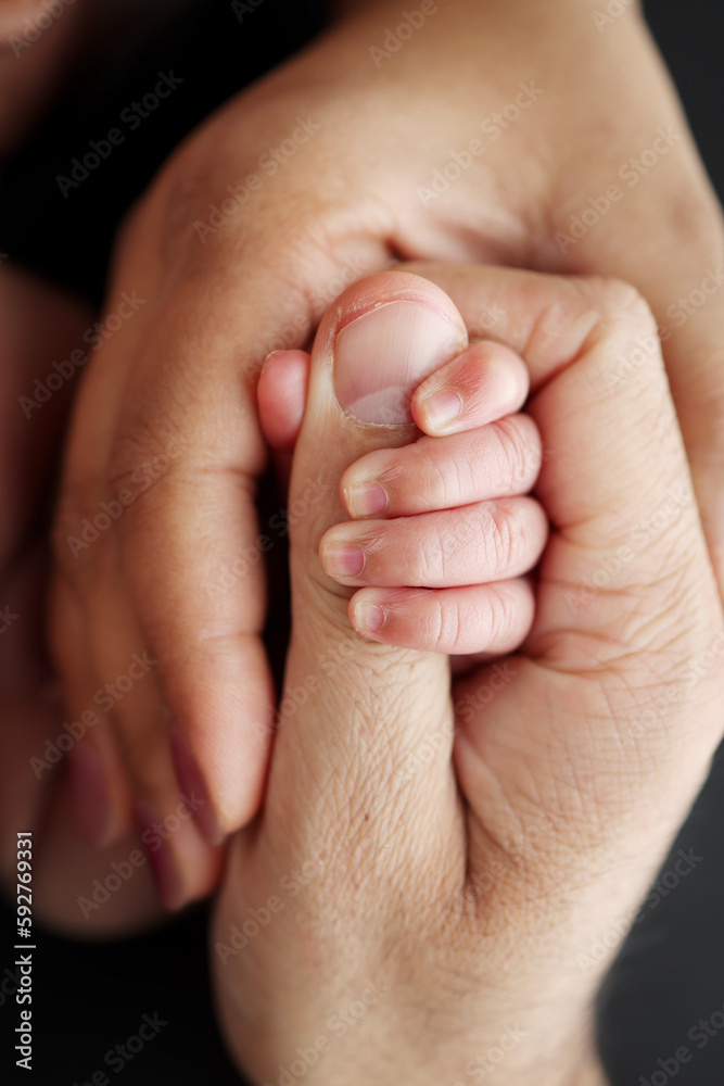 Close-up of the small hand of the child and the hand of the mother and father. A newborn baby after birth clings tightly to the finger of its parents. Professional macro photo on black background Close-up of the small hand of the child and the hand of the mother and father. A newborn baby after birth clings tightly to the finger of its parents. Professional macro photo on black background
