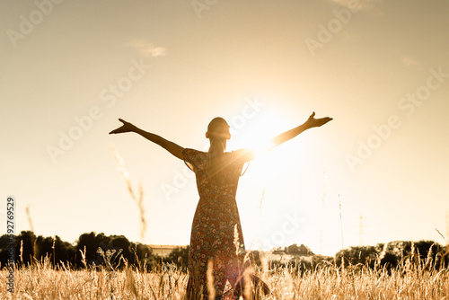 Joyful young woman with arms up to the sunlight feeling happy and free in nature 