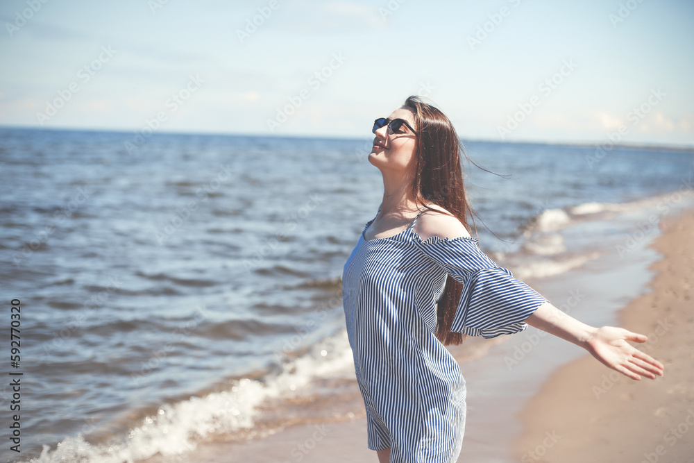 Happy smiling woman in free bliss on ocean beach standing with open hands. Portrait of a brunette female model in summer dress enjoying nature during travel holidays vacation outdoors Happy smiling woman in free bliss on ocean beach standing with open hands. Portrait of a brunette female model in summer dress enjoying nature during travel holidays vacation outdoors