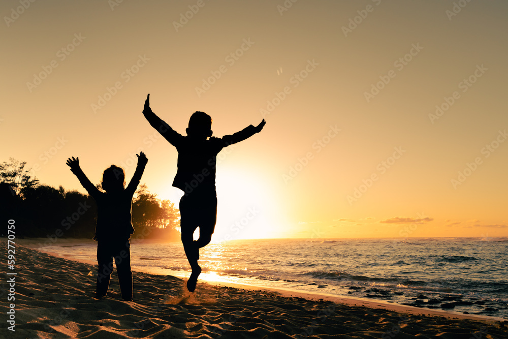 Fototapeta premium Happy little boy and girl kids playing jumping for joy on the beach having summertime fun 