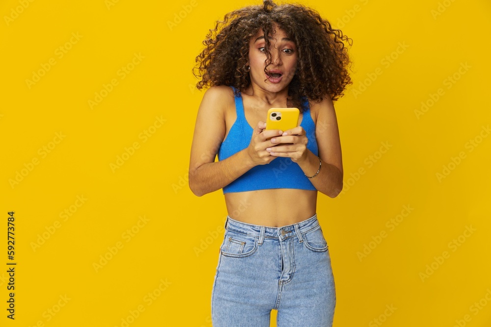 Influencer woman with phone in hand taking selfies talking on video call freelancer social media technology work, with curly afro hair in blue shirt yellow background , smile with teeth, copy space Influencer woman with phone in hand taking selfies talking on video call freelancer social media technology work, with curly afro hair in blue shirt yellow background , smile with teeth, copy space