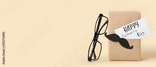 Glasses and gift for Father's Day celebration on beige background with space for text
