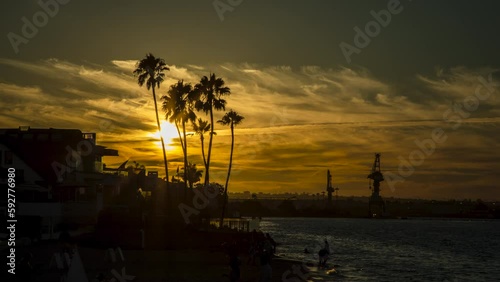 4K Timelapse of the sunset over Coronado Island in San Diego, California behind the silhouettes of palm trees and Navy vessels from the military naval bases nearby. 