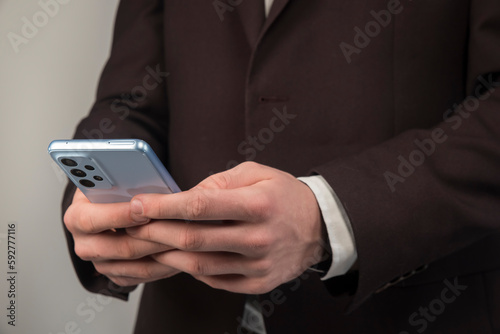 Mężczyzna w marynarce trzymający w dłoni telefon komórkowy.