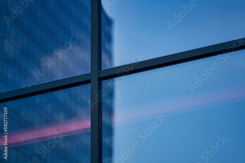 Ventana, forma de cruz, con reflejo rojo en la hora azul en edificio moderno en la ciudad
