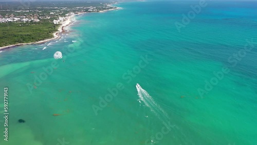 Aerial landscape view of an parasailing parachute inflight - pulled by a speedboat sailing in turquoise water near a tropical coastline - aerial video footage photo