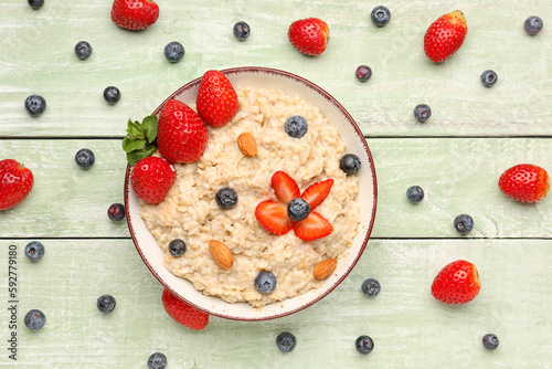 Bowl with tasty oatmeal, almonds, blueberries and strawberries on green wooden background