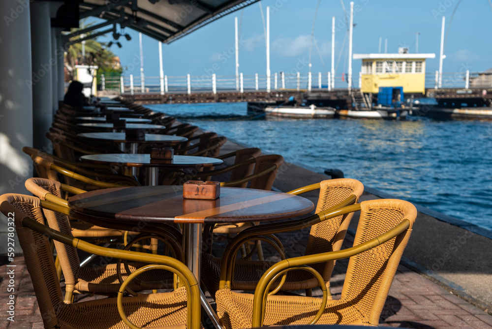 Tables of a cafe restaurant by the sea at the entrance to the bay of the port of Willemstad on the island of Curacao.