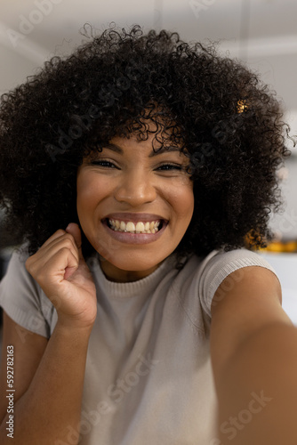 Portrait of happy, excited biracial woman with afro at home making video call and smiling