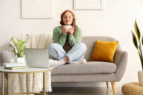 Beautiful redhead woman with cup of tea sitting on sofa at home