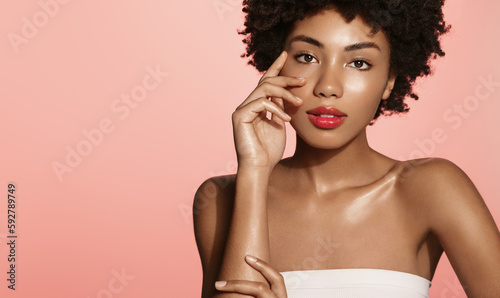 Beauty and health. Young african american woman with glowing face, touches her cheek and smiles, has moisturized facial skin without blemishes, concept of spa and cosmetology, pink background