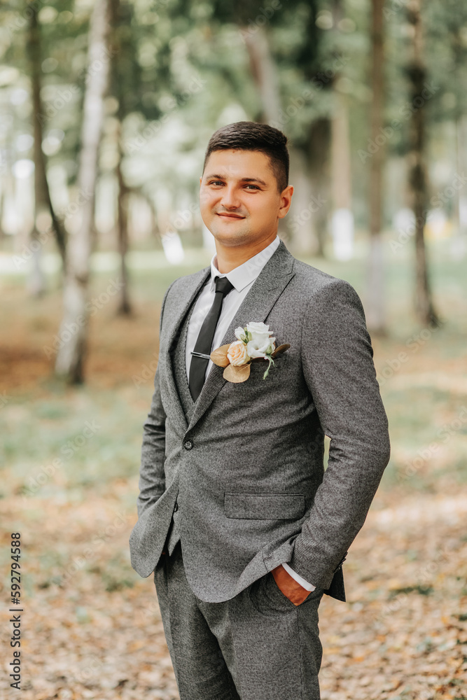 a stylish groom walks forward in the forest buttoning his jacket between tall trees. A fashionable groom, an adult man a stylish groom walks forward in the forest buttoning his jacket between tall trees. A fashionable groom, an adult man