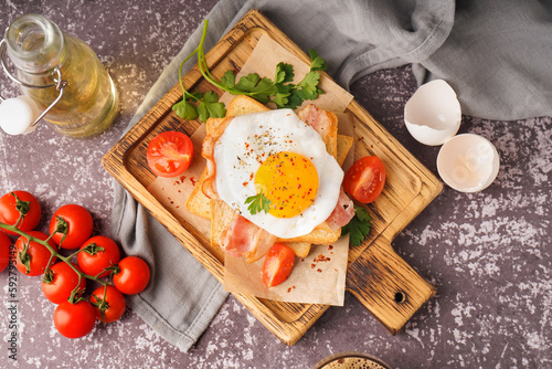 Delicious sandwich with fried egg, tomatoes and bacon on grunge grey background