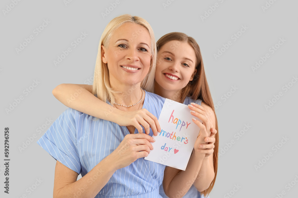 Young woman greeting her mother with card on grey background Young woman greeting her mother with card on grey background