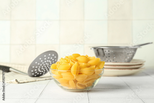 Bowl with raw conchiglie pasta on white tile background photo