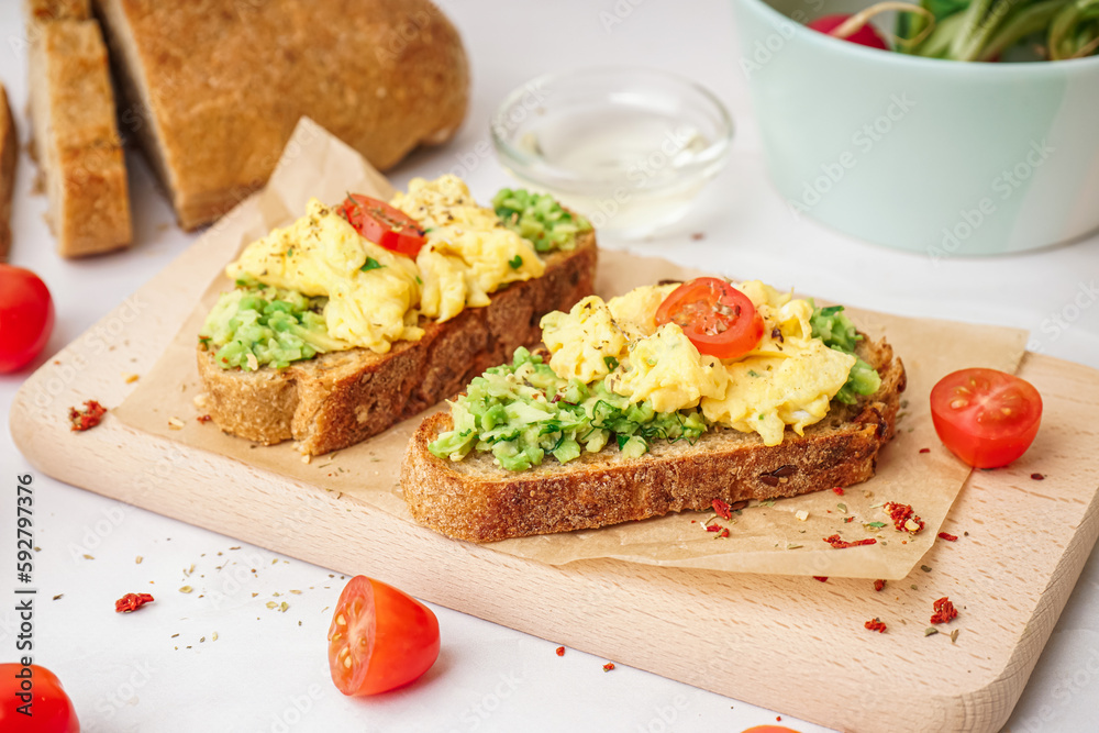 Wooden board with tasty scrambled eggs sandwich and vegetables on light background Wooden board with tasty scrambled eggs sandwich and vegetables on light background