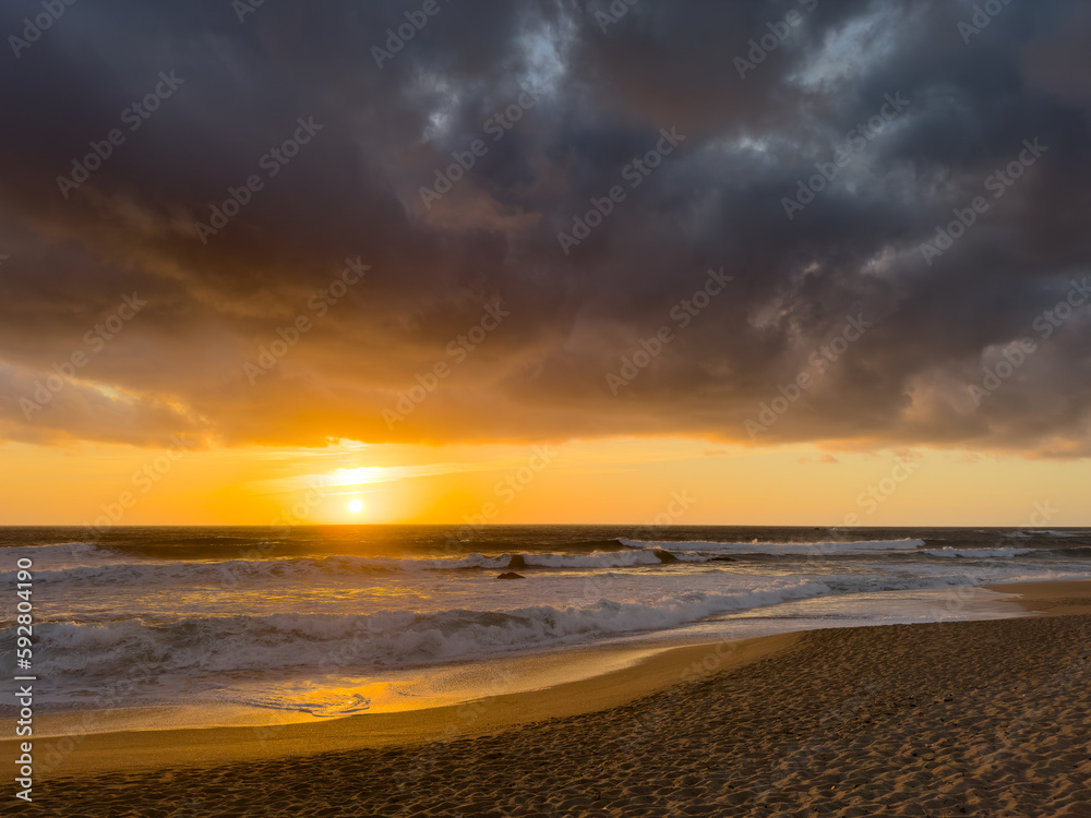 Dramatic sunset over Atlantic ocean in Portugal with dark, moody clouds in the sky