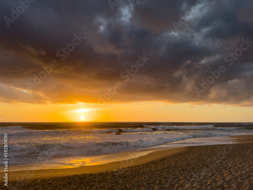 Dramatic sunset over Atlantic ocean in Portugal with dark, moody clouds in the sky