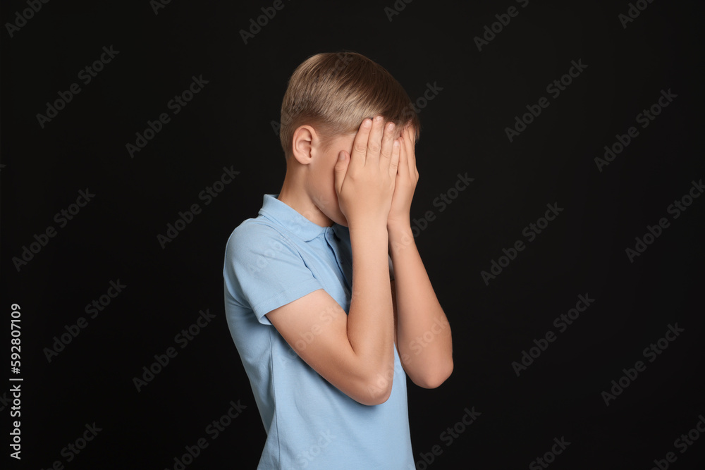 Boy covering face with hands on black background. Children's bullying Boy covering face with hands on black background. Children's bullying