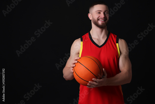 Athletic young man with basketball ball on black background. Space for text