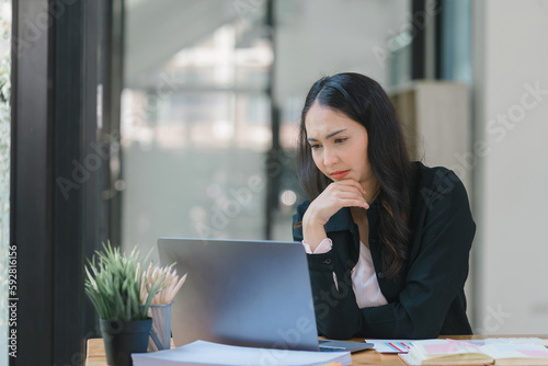 The stressed and exhausted millennial Asian businesswoman is tired after using a laptop while working remotely on a computer at a modern office. © kenchiro168