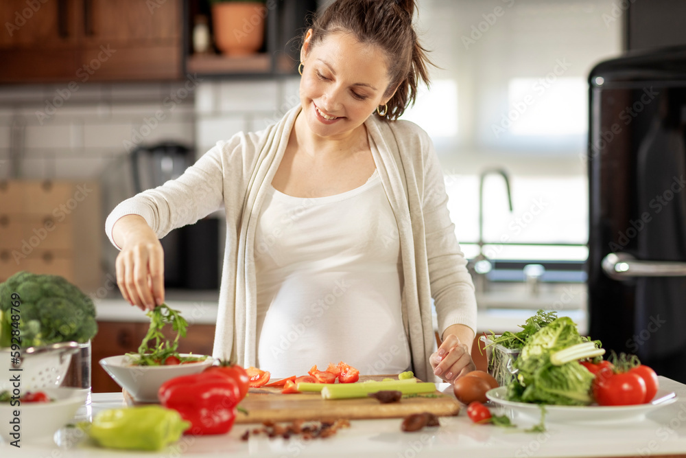Pregnant woman prepare healthy vegetarian food in the kitchen with smile