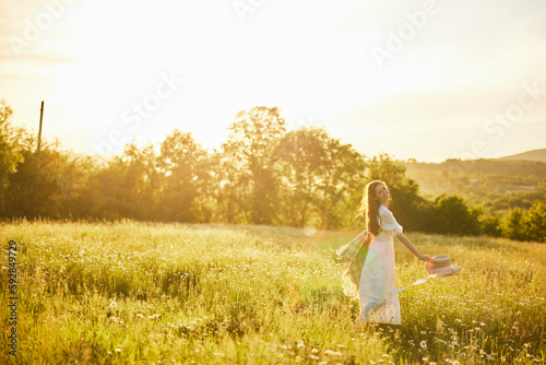 a woman in a light dress with a hat in her hands is spinning in nature in the rays of the setting sun © VICHIZH