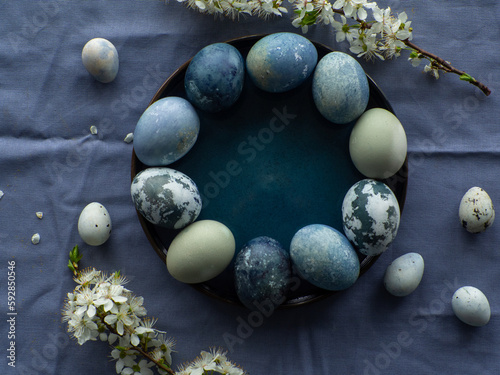 Blue painted easter eggs. Dyed Easter eggs with marble stone effect blue color on blue tablecloth background with cherry blossom twigs. Eggs background with copy space, Ester holiday postcard concept.