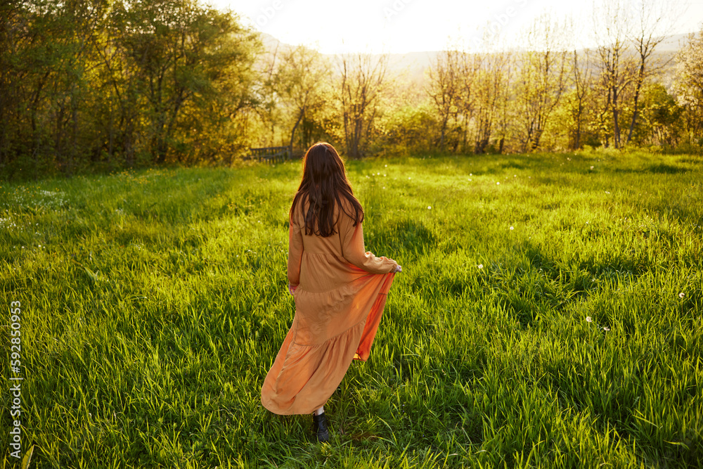 an attractive, slender, red-haired woman walks through a field during sunset, in a long orange dress enjoying unity with nature and relaxation holding the edge of her clothes an attractive, slender, red-haired woman walks through a field during sunset, in a long orange dress enjoying unity with nature and relaxation holding the edge of her clothes
