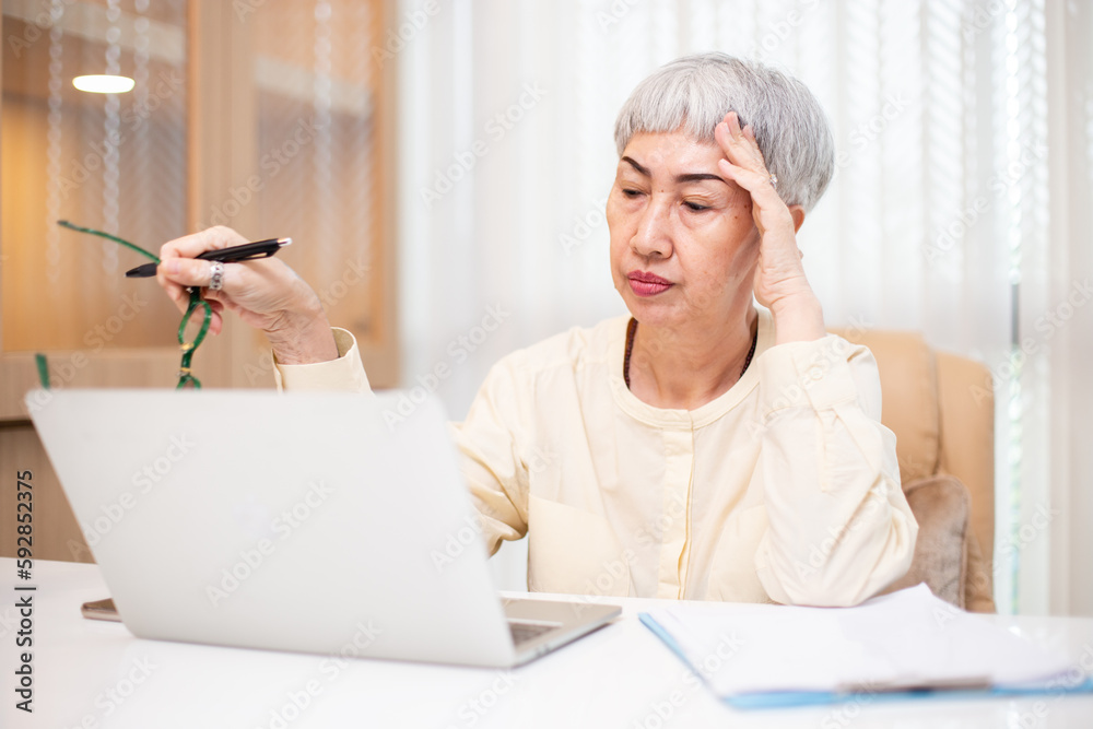 Working in retirement concept, Asian senior business woman stress from hard work, Female manager headache sitting at table with laptop. Worried middle aged female health problems. Working in retirement concept, Asian senior business woman stress from hard work, Female manager headache sitting at table with laptop. Worried middle aged female health problems.