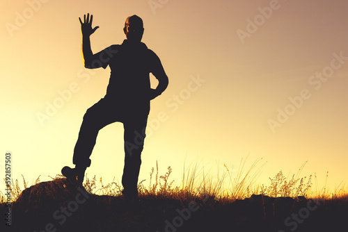 the silhouette of a man outside the room against the background of the sunset, raising his palm up in greeting