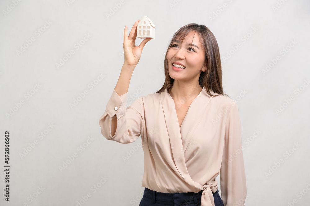 Obraz premium Young smiling woman holding small model house over white background studio.